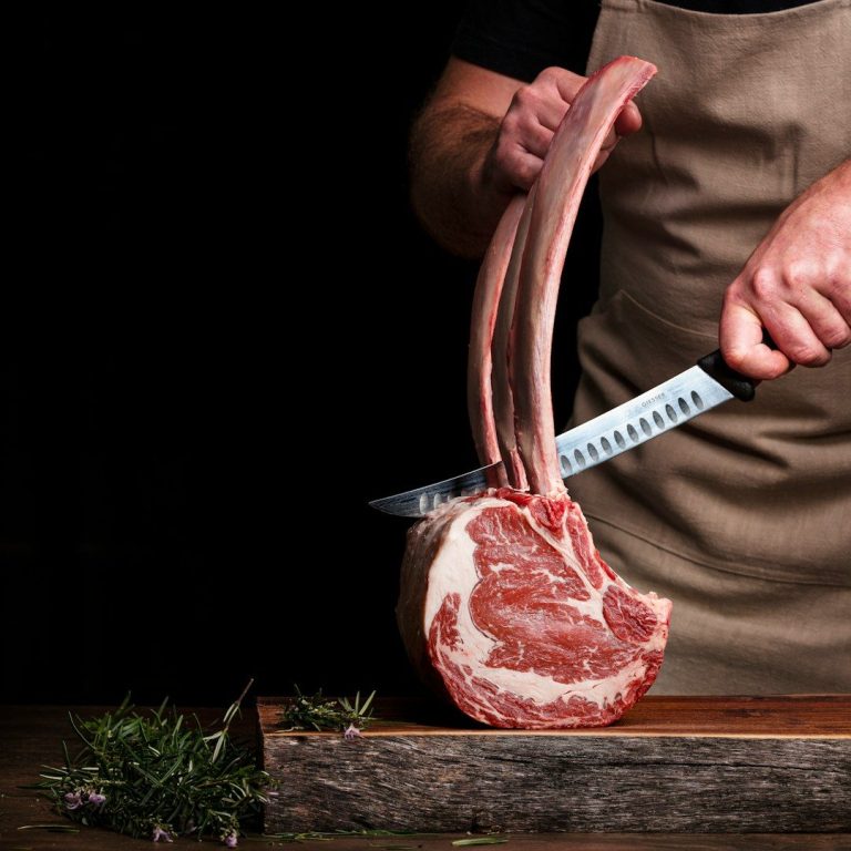 Tomahawk de bœuf Un boucher tranche une côte de bœuf sur une planche en bois.